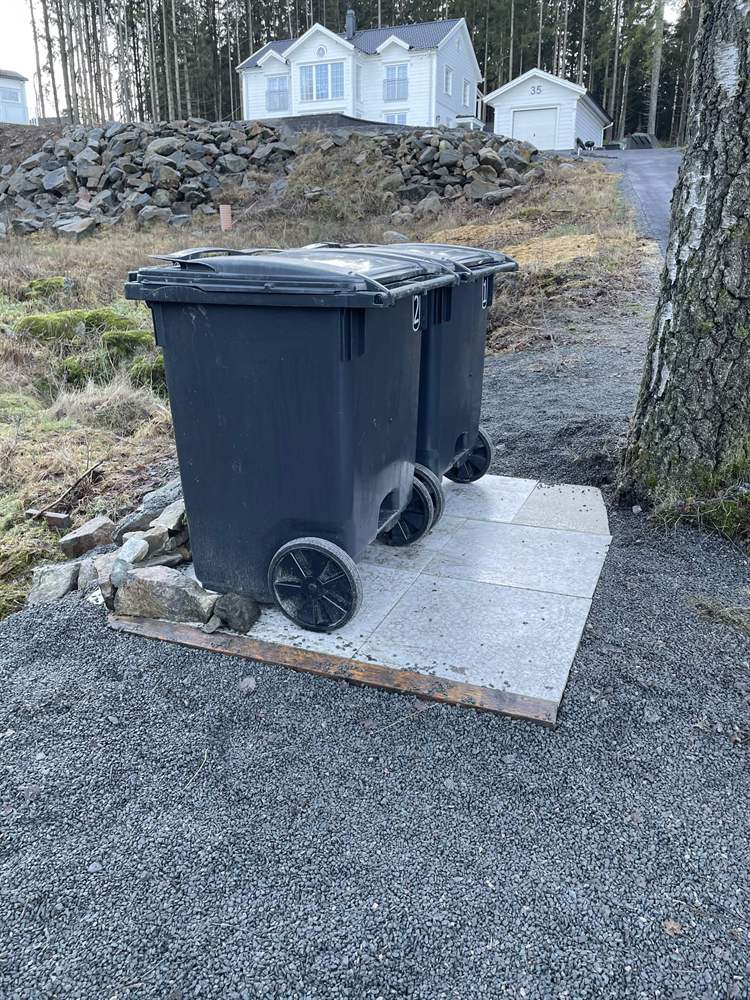 Två sopkärl på plan yta av stenplattor med naturstensmur bakom