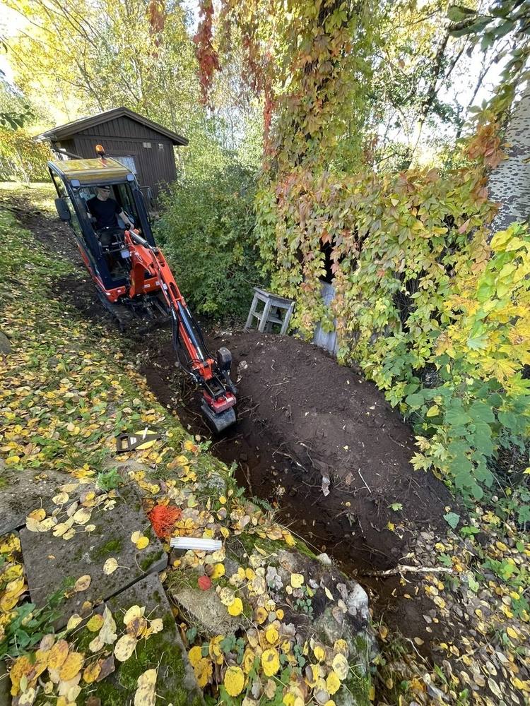 Minigrävare gräver dike för stödmur